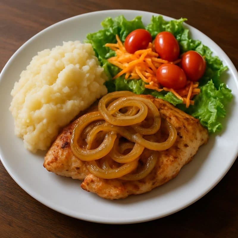 Filete de pollo encebollado acompañado de puré de yuca y ensalada